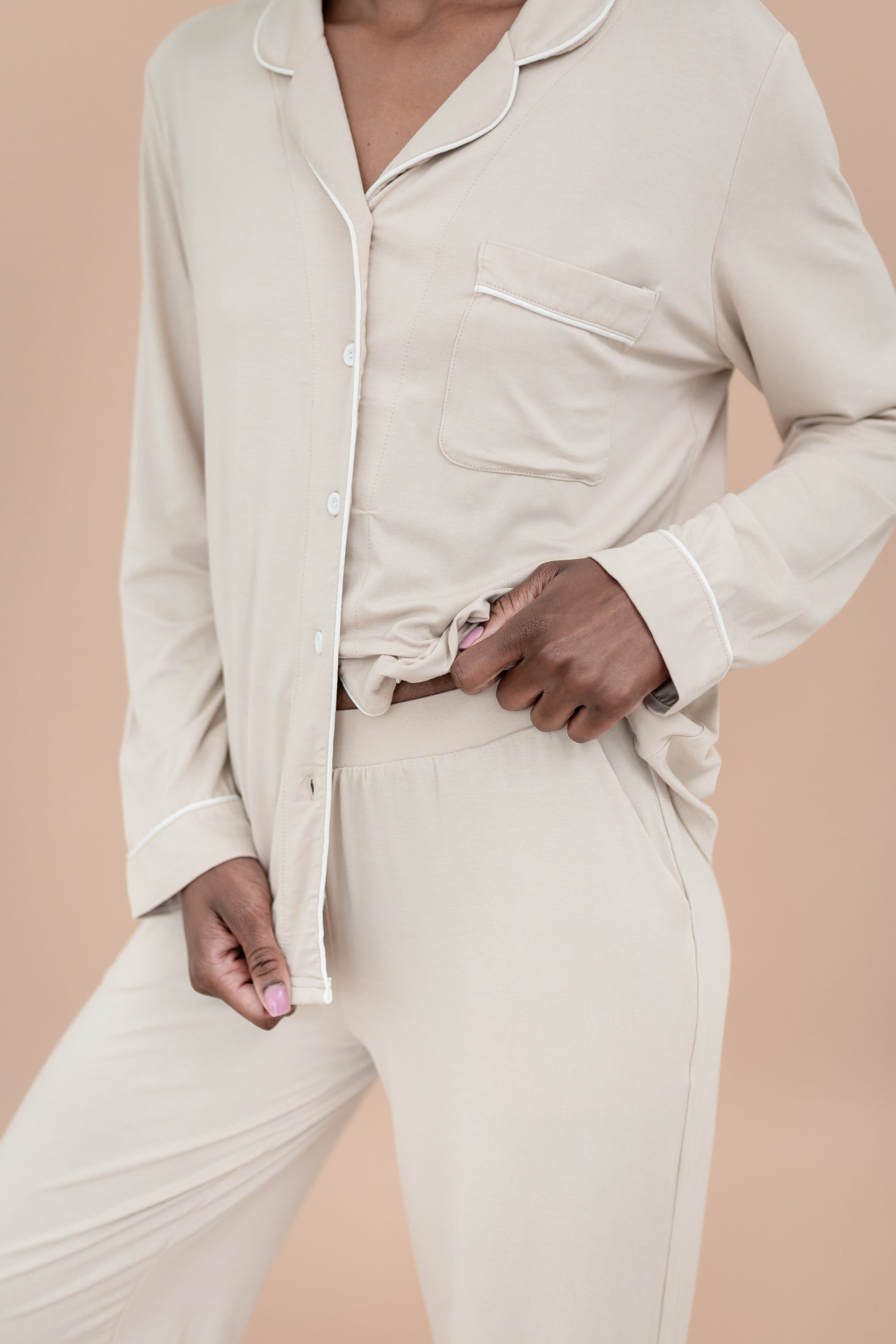 Person wearing a beige button-up pajama shirt and pants against a beige background