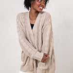 Model holding her arms across her front while wearing the Kyte Chunky Knit Cable Cardigan in Almond