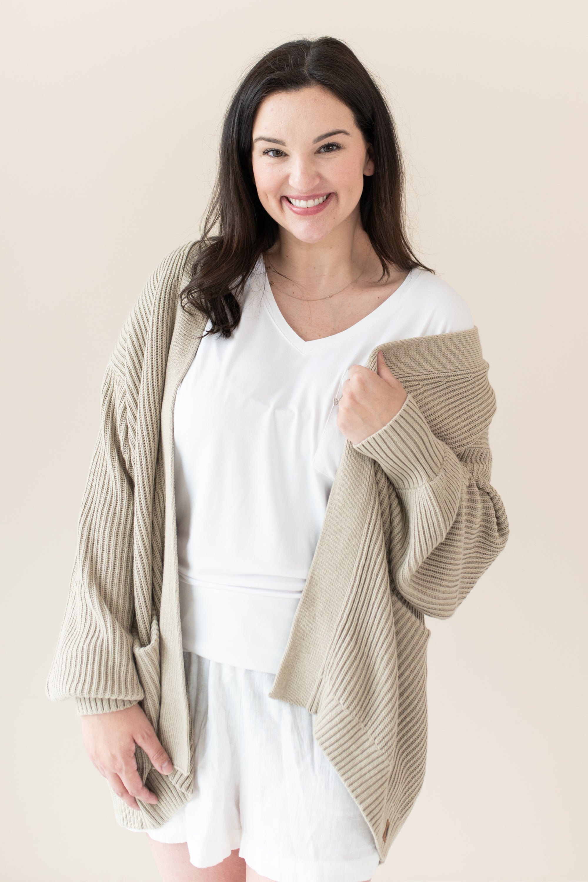 Woman in white outfit modeling Chunky Knit Women's Oversized Cardigan in Almond holidng sweater