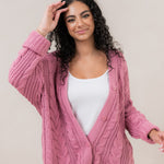 Model with hand in her hair while wearing the  Kyte Cable Knite Cardigan in Apple Blossom paired with jeans