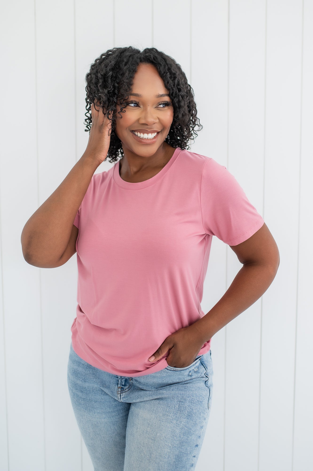 Model smiling to the side with one hand in hair while wearing the Kyte Crew Neck Tee in Apple Blossom