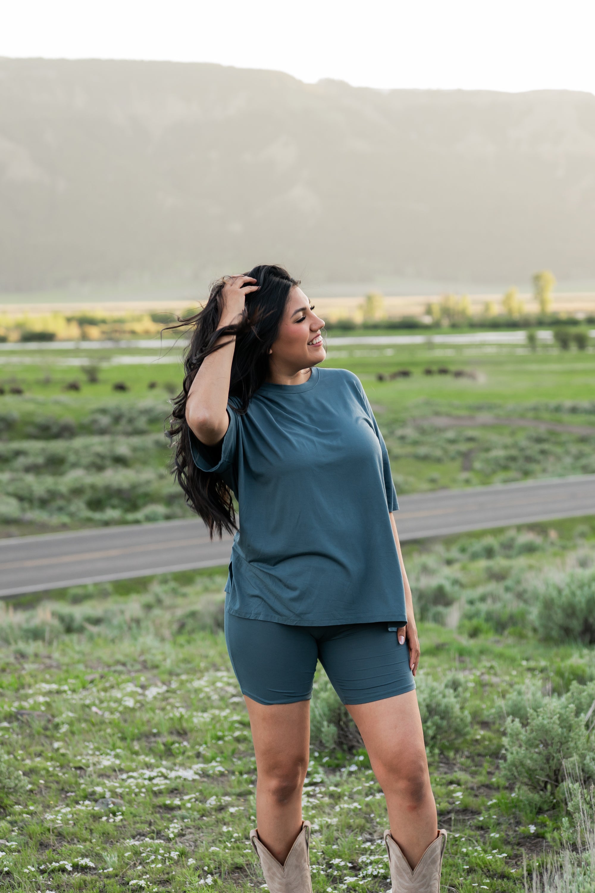 Model in a grassy field looking away with her hand in her hair while wearing Women's Biker Short Set in Atlantic