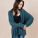 Model looking to the side with unbuttoned Chunky Cable Knit Cardigan in Atlantic paired with jeans