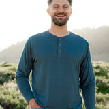Smiling model in front of a grassy background while wearing a Kyte Long Sleeve Henley in Atlantic