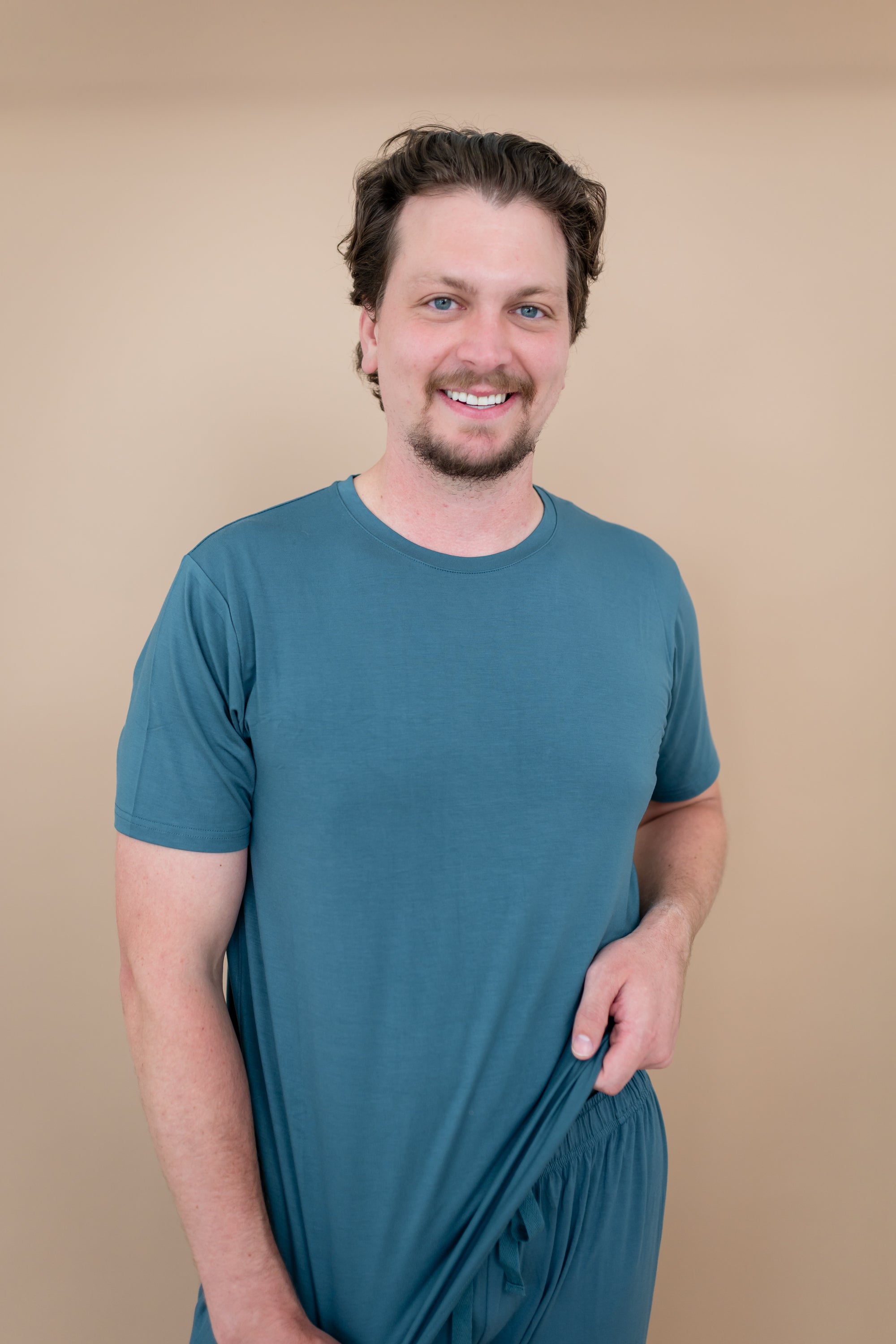 Smiling model wearing Men's Crew Neck Tee in Atlantic with hands at bottom hem