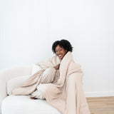 Smiling model sitting on a white couch while wrapped in a Blanket in Bisque