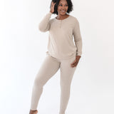 Smiling female standing with one hand in her hair and the other hand in the pants pocket of the Women’s Ribbed Henley Set in Bisque