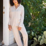 Female model leaning against a white house wearing the Long-Sleeved Women's Pajama Set in Bisque with Bisque Trim