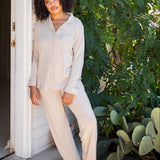 Female model leaning against a white house wearing the Long-Sleeved Women's Pajama Set in Bisque with Bisque Trim