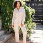 Female standing outside in front of greenery wearing the Long-Sleeved Women's Pajama Set in Bisque with Bisque Trim