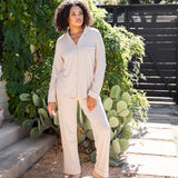 Female standing outside in front of greenery wearing the Long-Sleeved Women's Pajama Set in Bisque with Bisque Trim