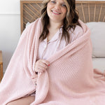 Model sitting in bed with the Chunky Knit Throw Blanket in Blush wrapped around her