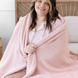 Model sitting in bed with the Chunky Knit Throw Blanket in Blush wrapped around her