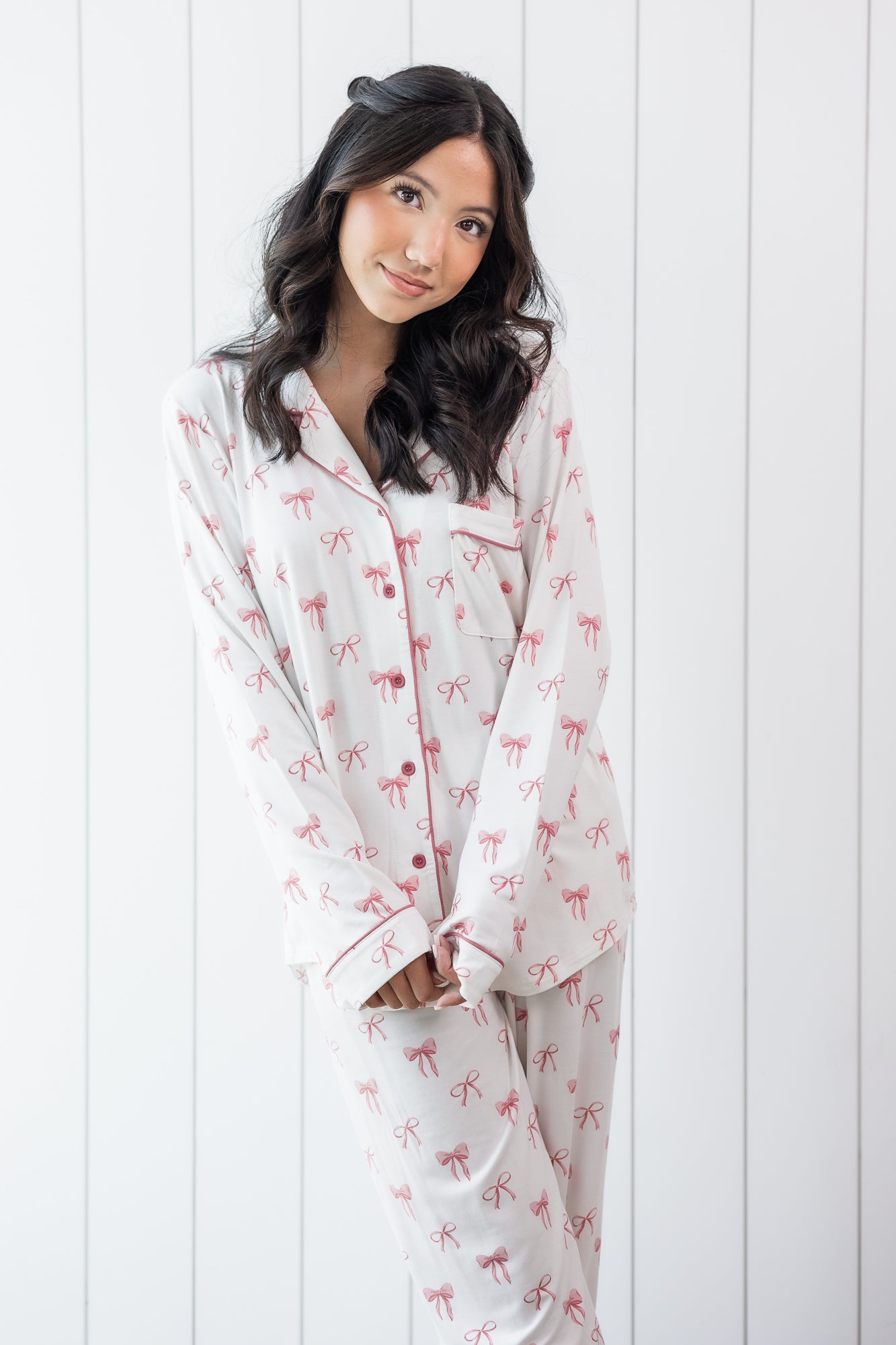 Woman modeling white long sleeve button up pajama set with pink bow print and pink piping