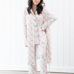 Woman wearing a white pajama set with pink bow patterns in a room with white walls and wooden floor.