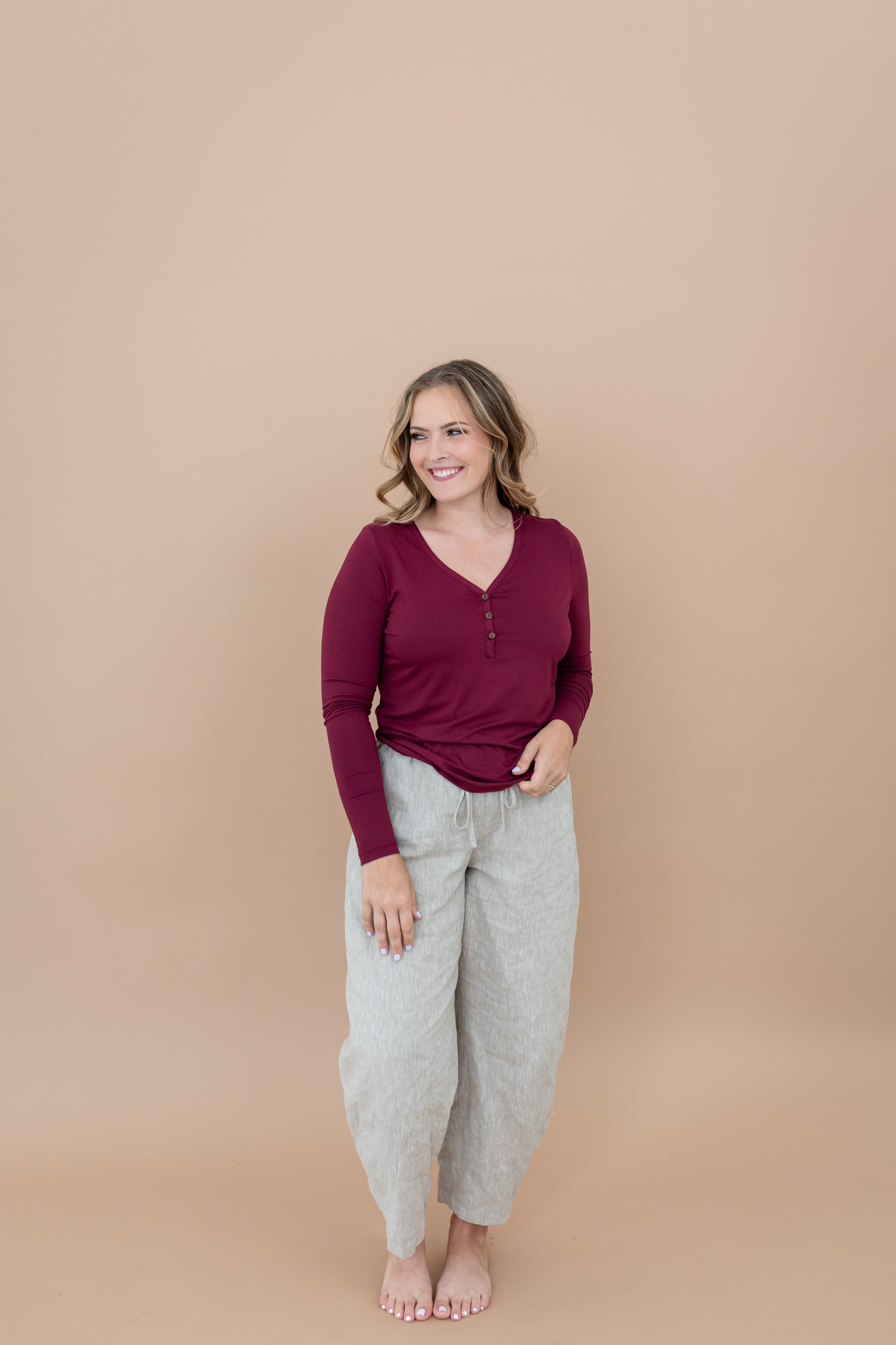 Smiling model looking to the side Model looking to the side while wearing the Women's Henley top in Burgundy paired with light bottoms