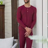 Male model leaning against a white house looking off to the side wearing the Men's Ribbed Henley Set in Burgundy
