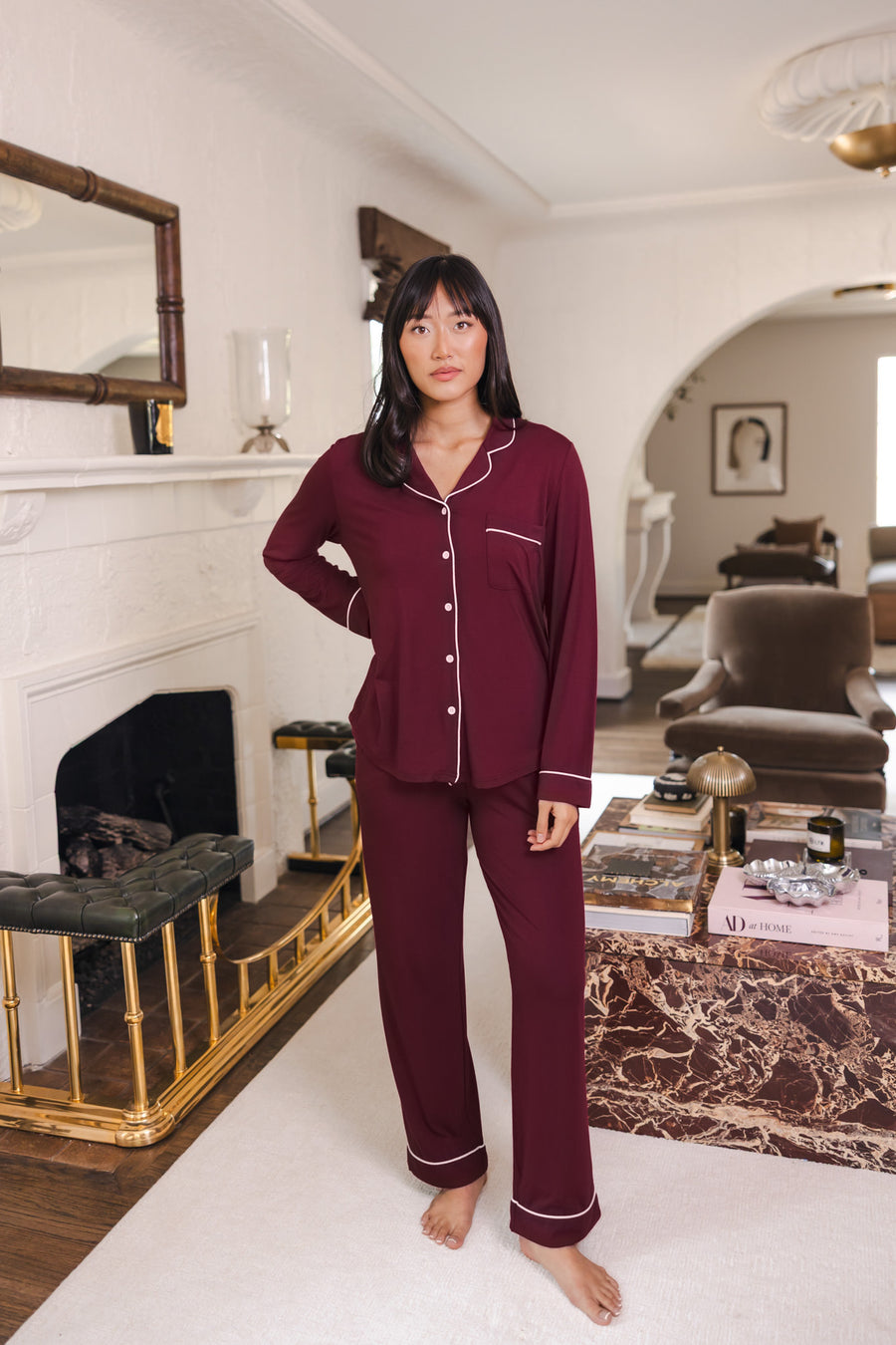 Woman wearing long sleeve burgundy pajama set with white piping in a luxury living room