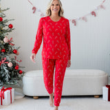 Smiling female model walking away from two decorated christmas trees and a beige ottoman wearing the Women's Jogger Pajama Set in Candy Cane