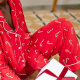 Close up of model sitting on the floor and holding a gift while wearing the Bamboo Long-Sleeved Women's Pajama Set in Candy Cane