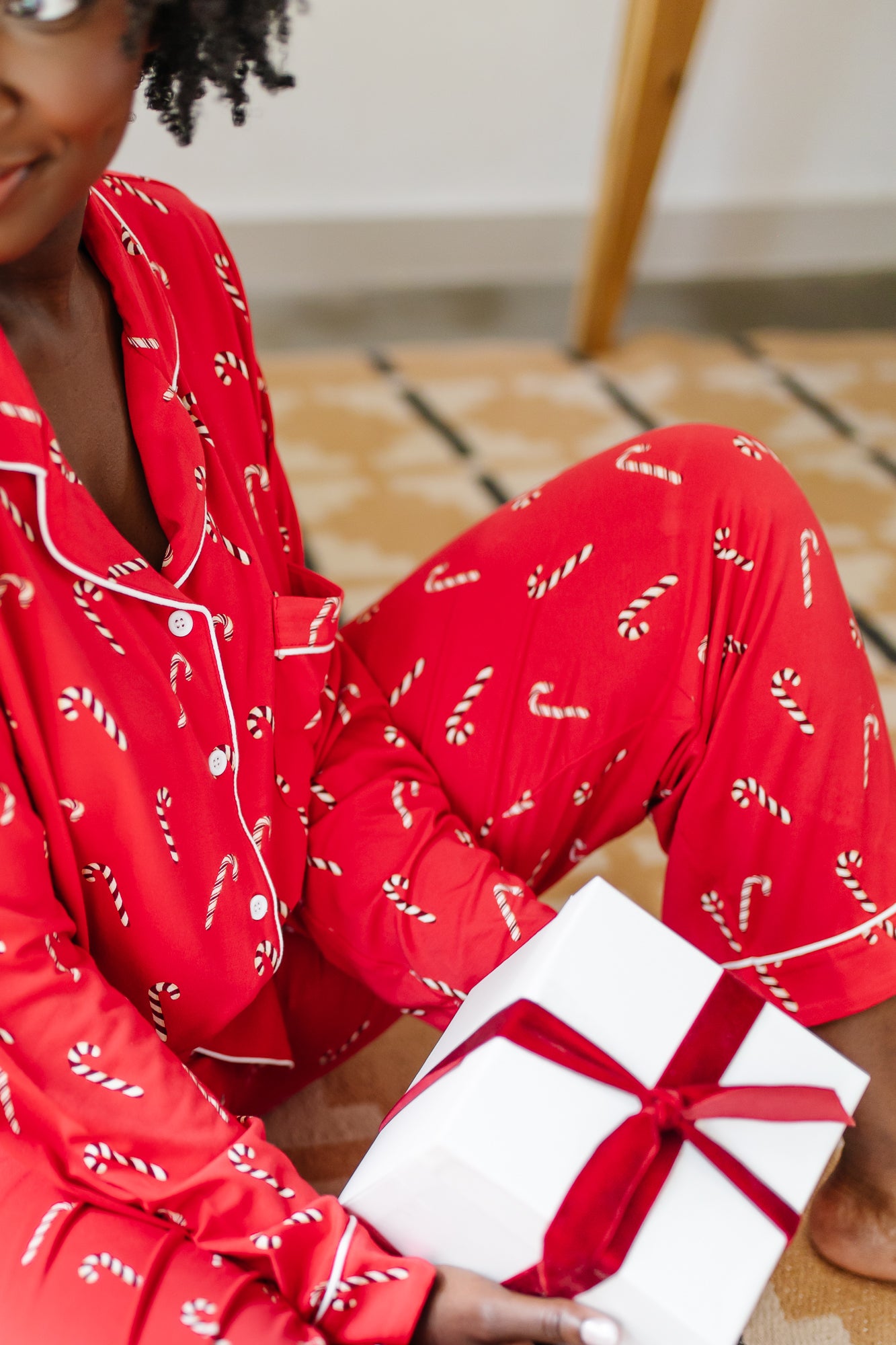 Close up of model sitting on the floor and holding a gift while wearing the Bamboo Long-Sleeved Women's Pajama Set in Candy Cane