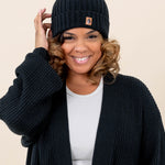 Smiling model wearing the Chunky Knit Adult Ribbed Beanie in Midnight paired with a white shirt and Midnight  Chunky Knit oversized women's Cardigan