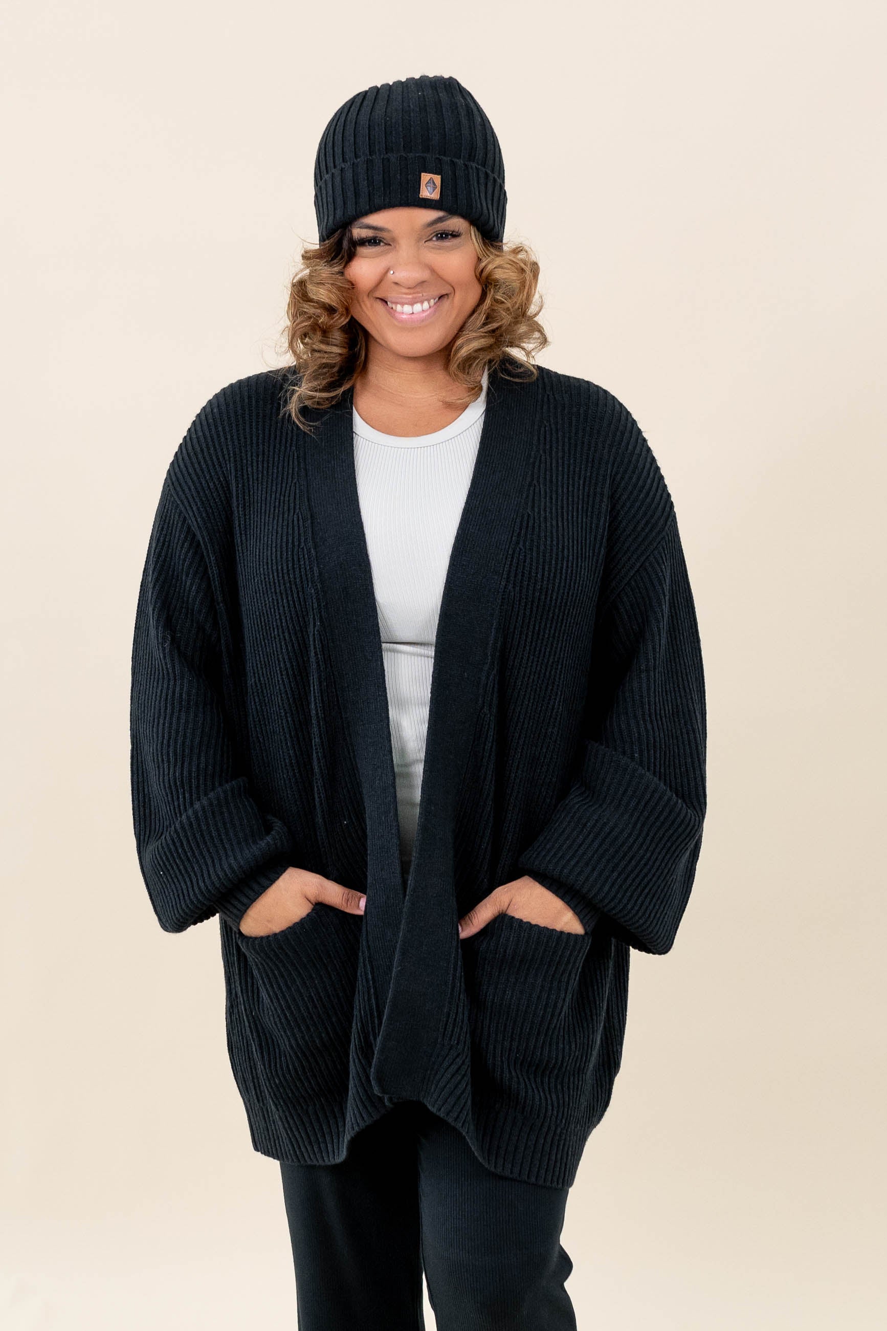Female modeling the Chunky Knit Women's Oversized Cardigan in Midnight wearing a white shirt, black pants and Midnight Beanie