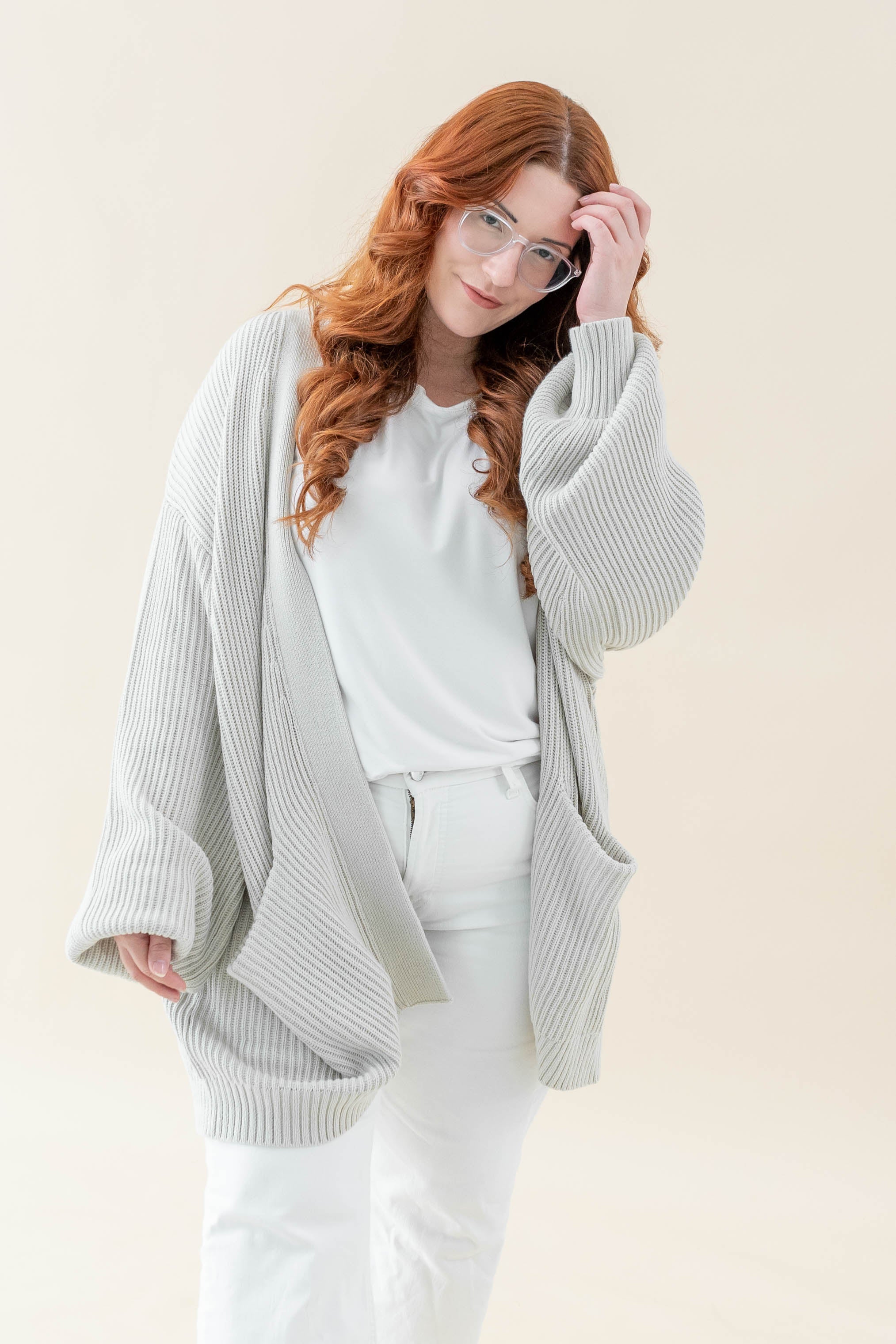 Female modeling the Chunky Knit Women's Oversized Cardigan in Oat paired with a white shirt and white pants