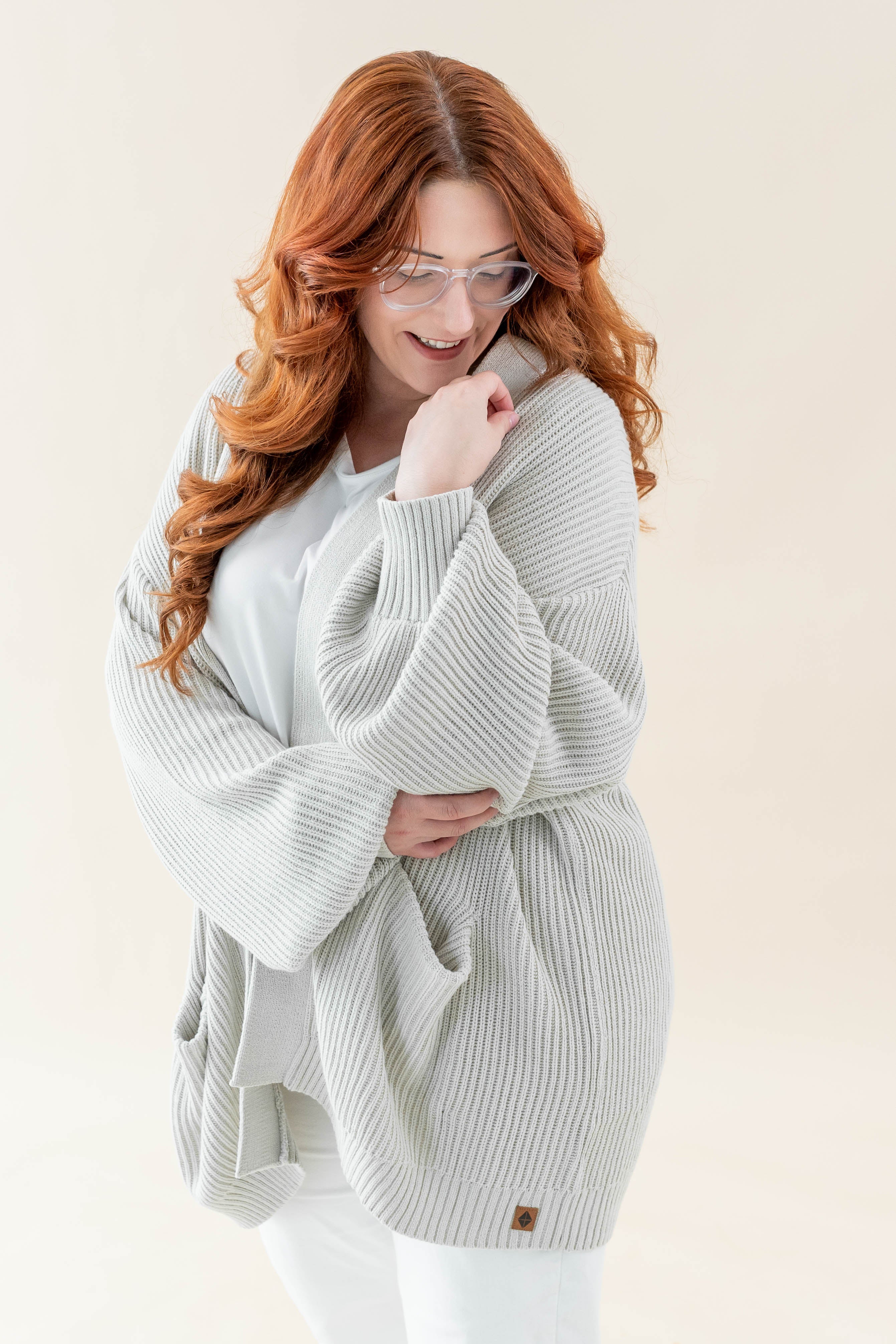 Female wearing the Chunky Knit Women's Oversized Cardigan in Oat paired with a white shirt and white pants