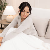 Model sitting in bed with the Adult Quilted Blanket in Cloud 2.5 overtop her legs