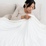 Model lying in bed holding the Adult Quilted Blanket in Cloud 1.0