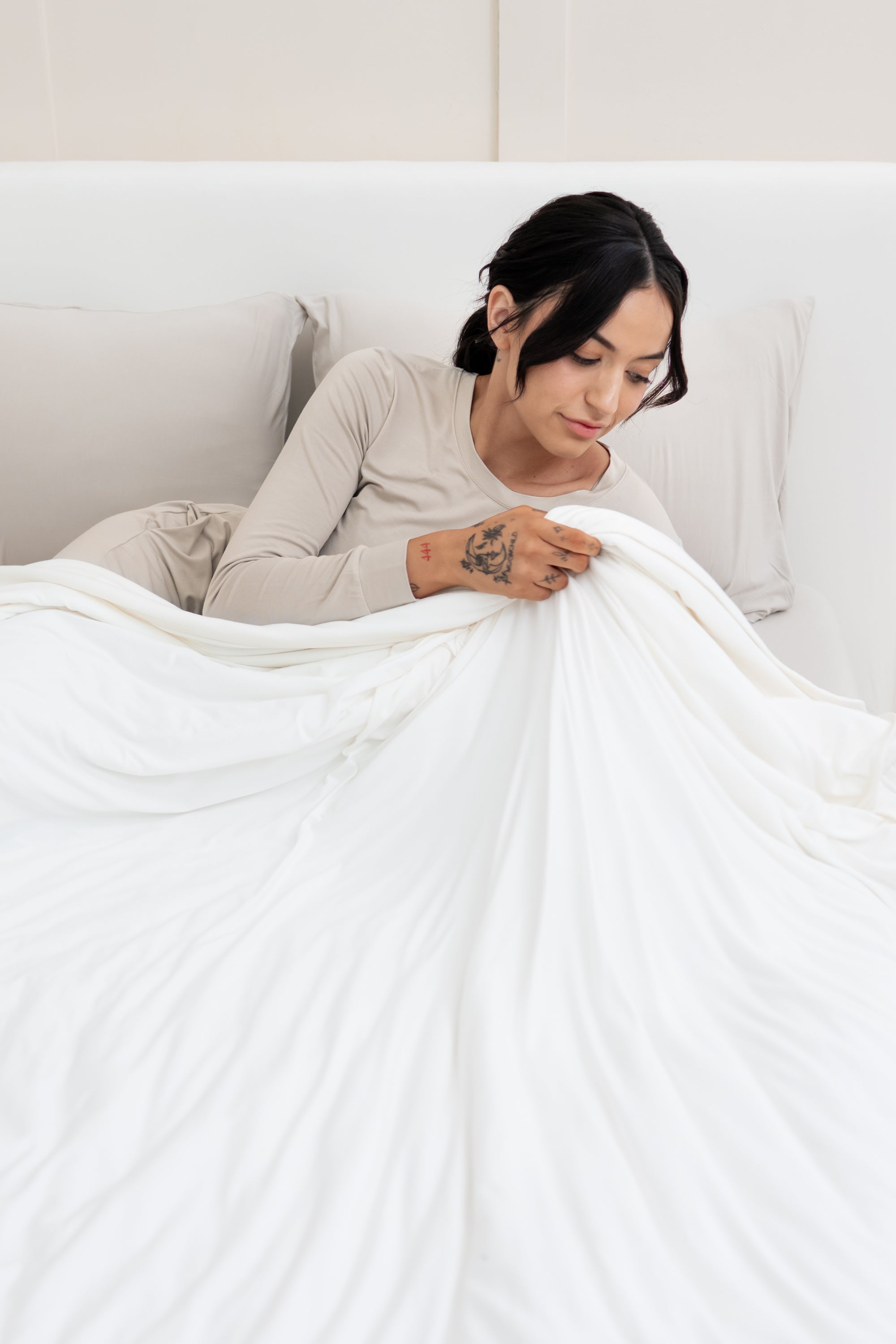 Model lying in bed holding the Adult Quilted Blanket in Cloud 1.0