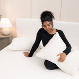 Model sitting on the bed holding a pillow in a Cloud Pillowcase on top of the Fitted Sheet in Cloud