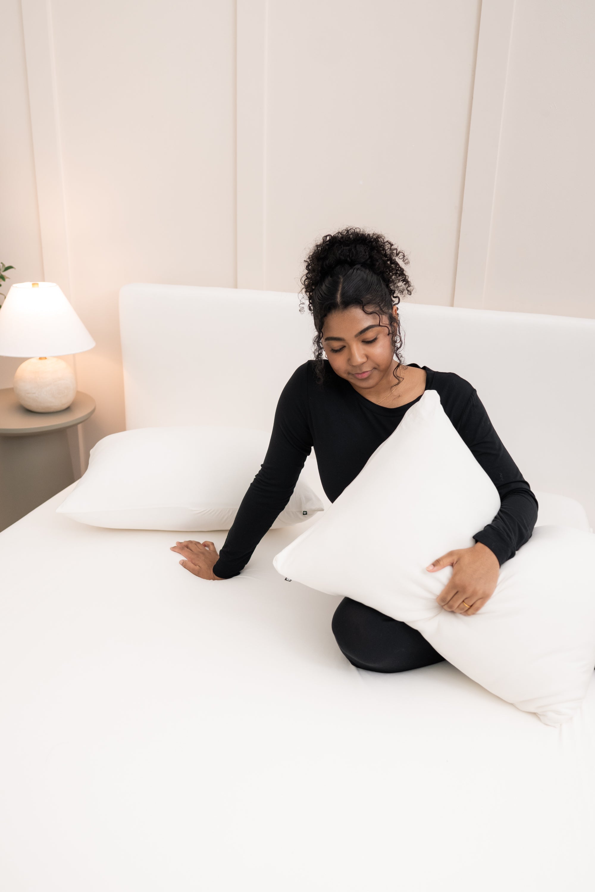 Model sitting on the bed holding a pillow in a Cloud Pillowcase on top of the Fitted Sheet in Cloud