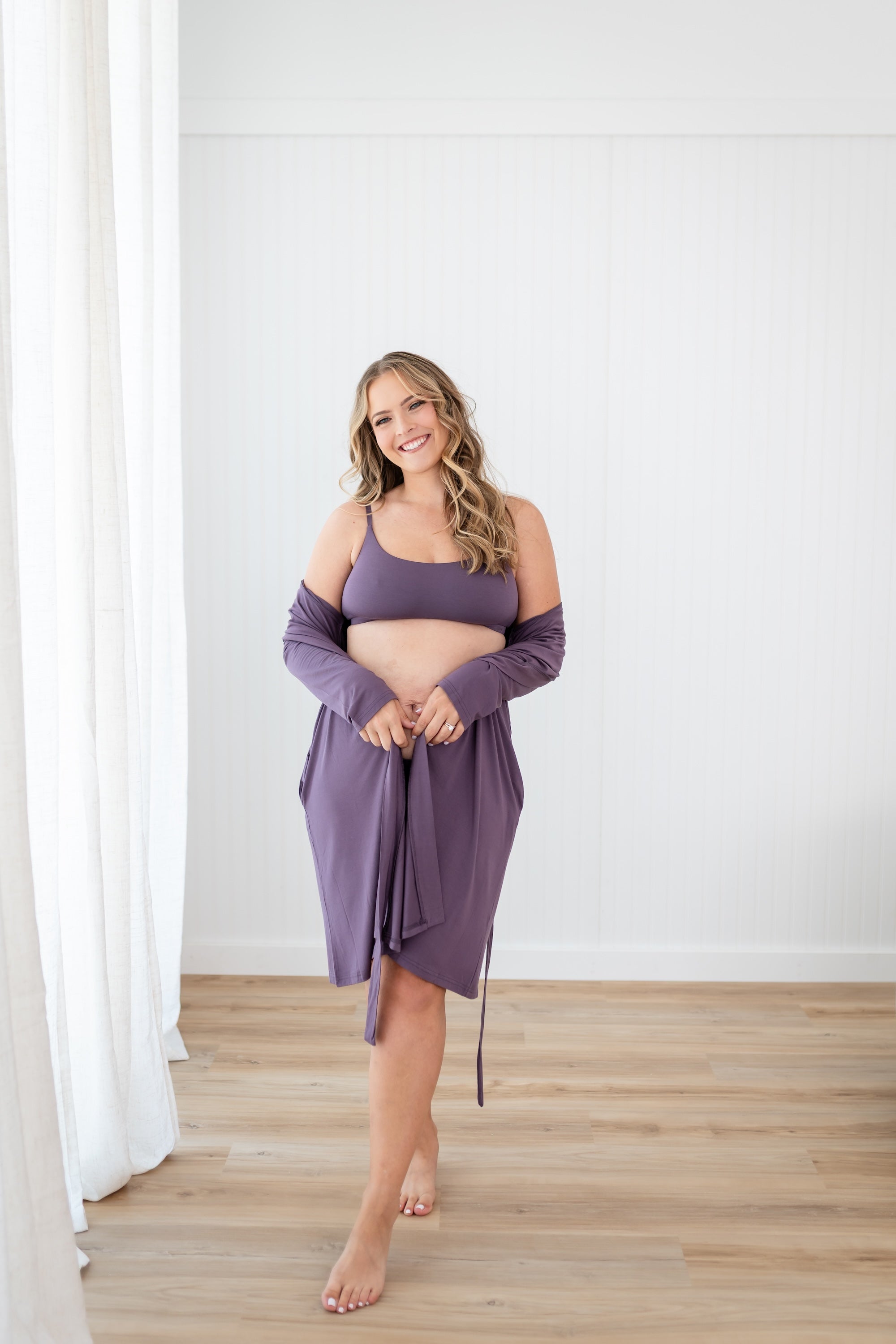 Woman wearing Scoop Neck Bralette in Currant and lounge robe standing in a room with white walls and wooden floor.