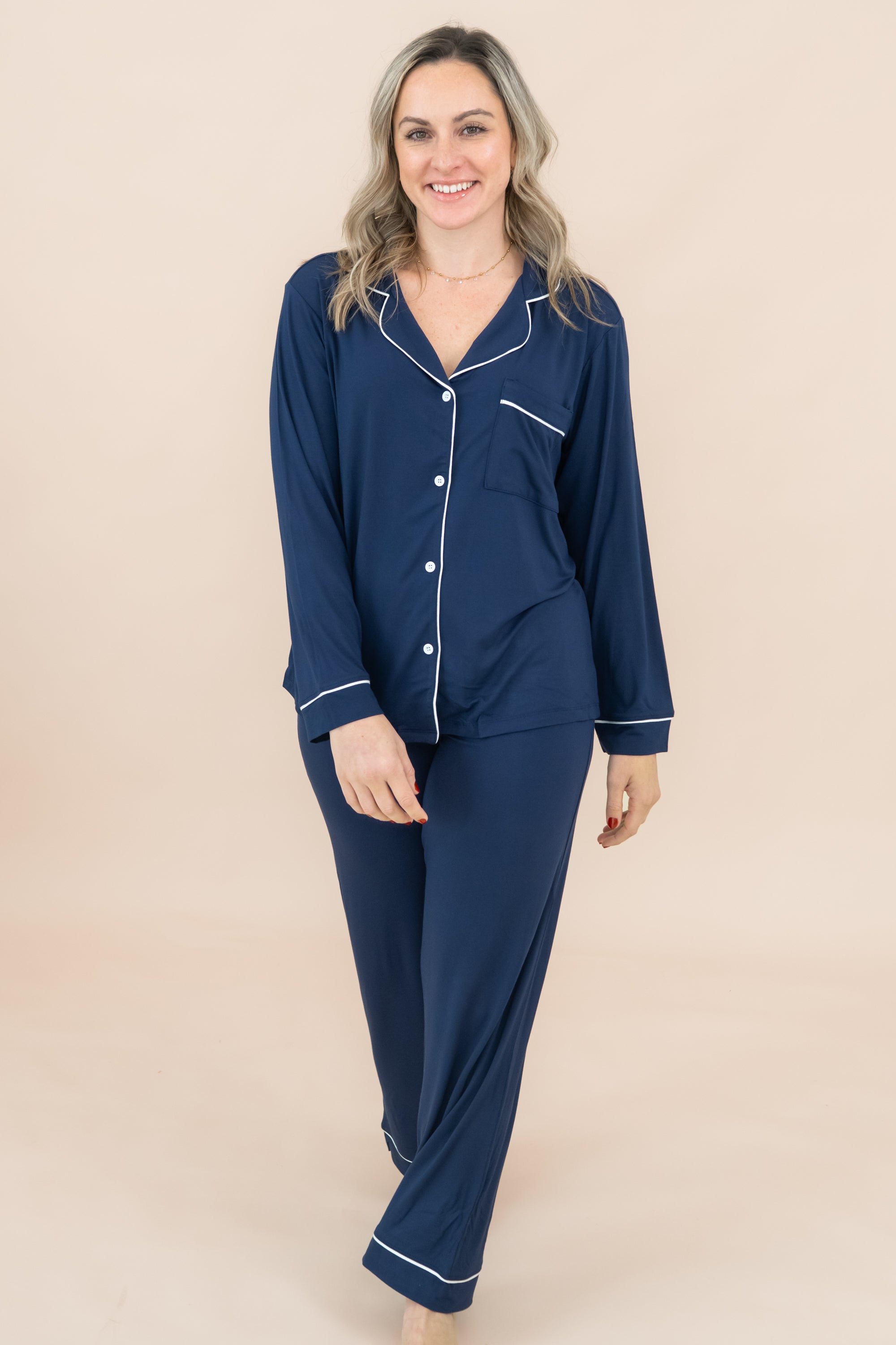 Woman wearing a navy blue pajama set with white buttons on a beige background