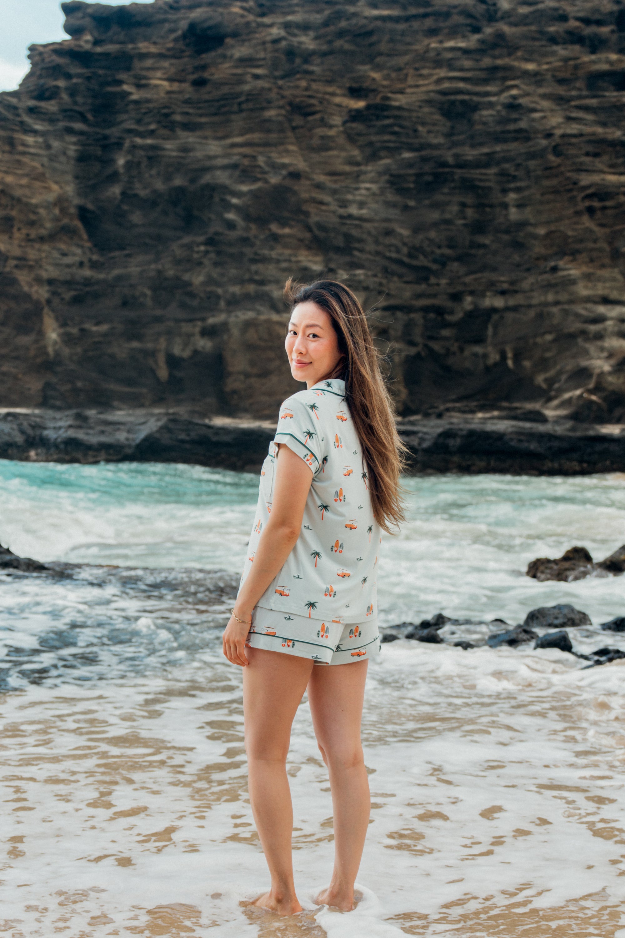 Woman standing on a beach with ocean and cliffs in the background wearing Women's Short Sleeve Pajama Set in Dew Surf