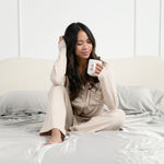 Female model sitting in bed on the Bamboo Sateen Sheet Set in Dove Gray holding a cup of coffee