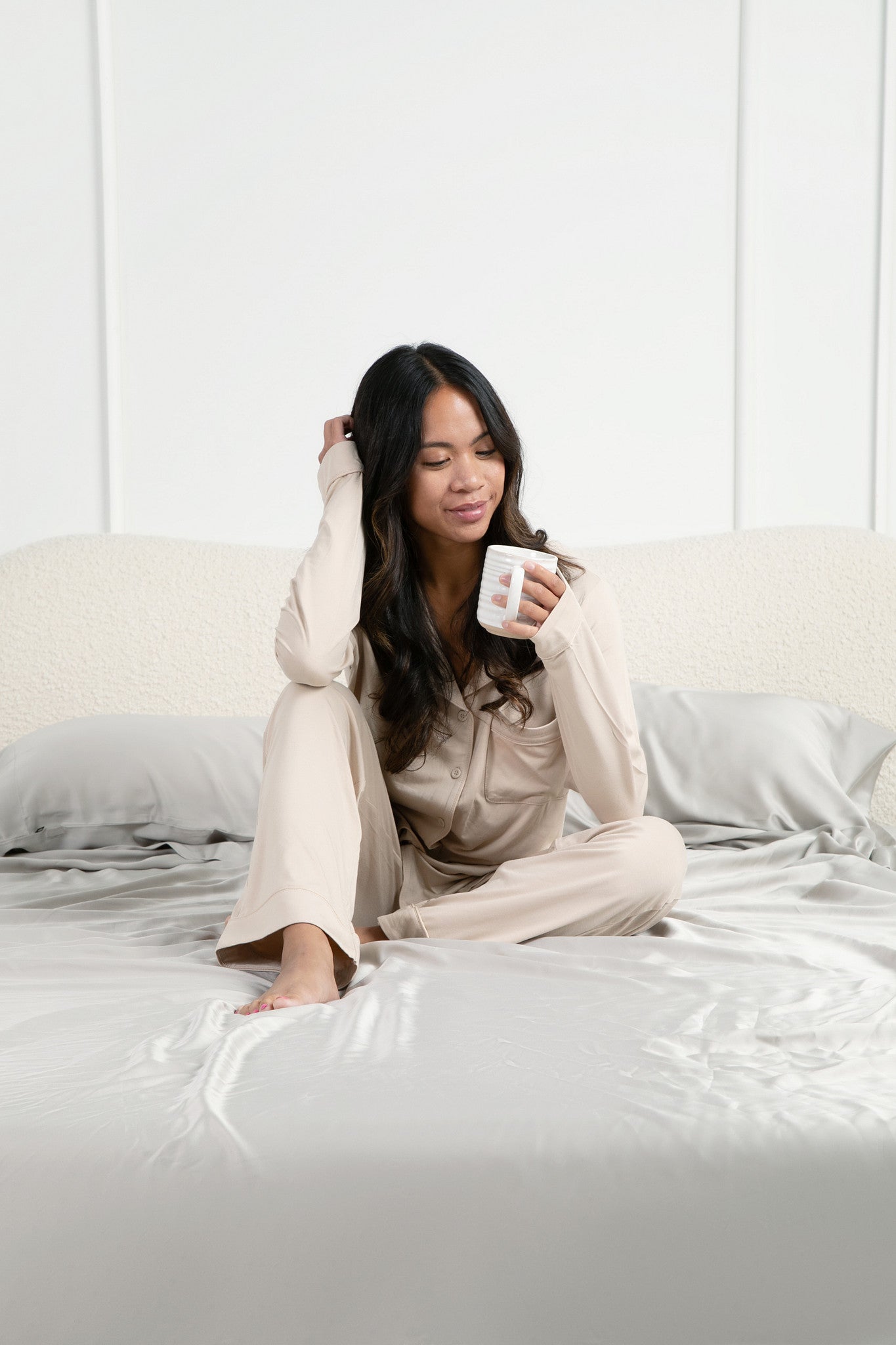 Female model sitting in bed on the Bamboo Sateen Sheet Set in Dove Gray holding a cup of coffee