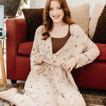 Smiling sitting woman sitting on the floor modeling the Kyte Women's Lounge Robe in Espresso Martini