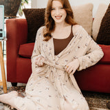 Smiling sitting woman sitting on the floor modeling the Kyte Women's Lounge Robe in Espresso Martini