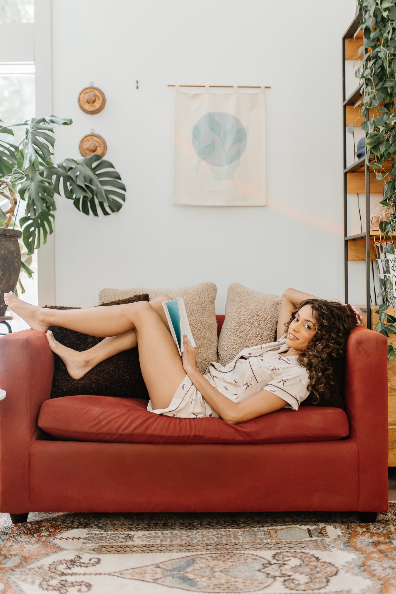 Model laying on a red couch reading while wearing the Bamboo Women's Short Sleeve Pajama Set in Espresso Martini