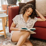 Model sitting on the floor reading a book wearing the Kyte Bamboo Women's Short Sleeve Pajama Set in Espresso Martini