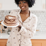 Smiling model holding a cake and modeling the Bamboo Long-Sleeved Women's Pajama Set in Espresso Martini