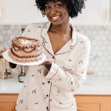 Smiling model holding a cake and modeling the Bamboo Long-Sleeved Women's Pajama Set in Espresso Martini