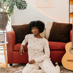 Model sitting in front of a red sofa modeling the Bamboo Women's Jogger Pajama Set in Espresso Martini