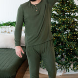 Male mode walking with one hand up behind his head wearing the Men's Ribbed Henley Set in Fir beside a bed and in front of a lit Christmas tree