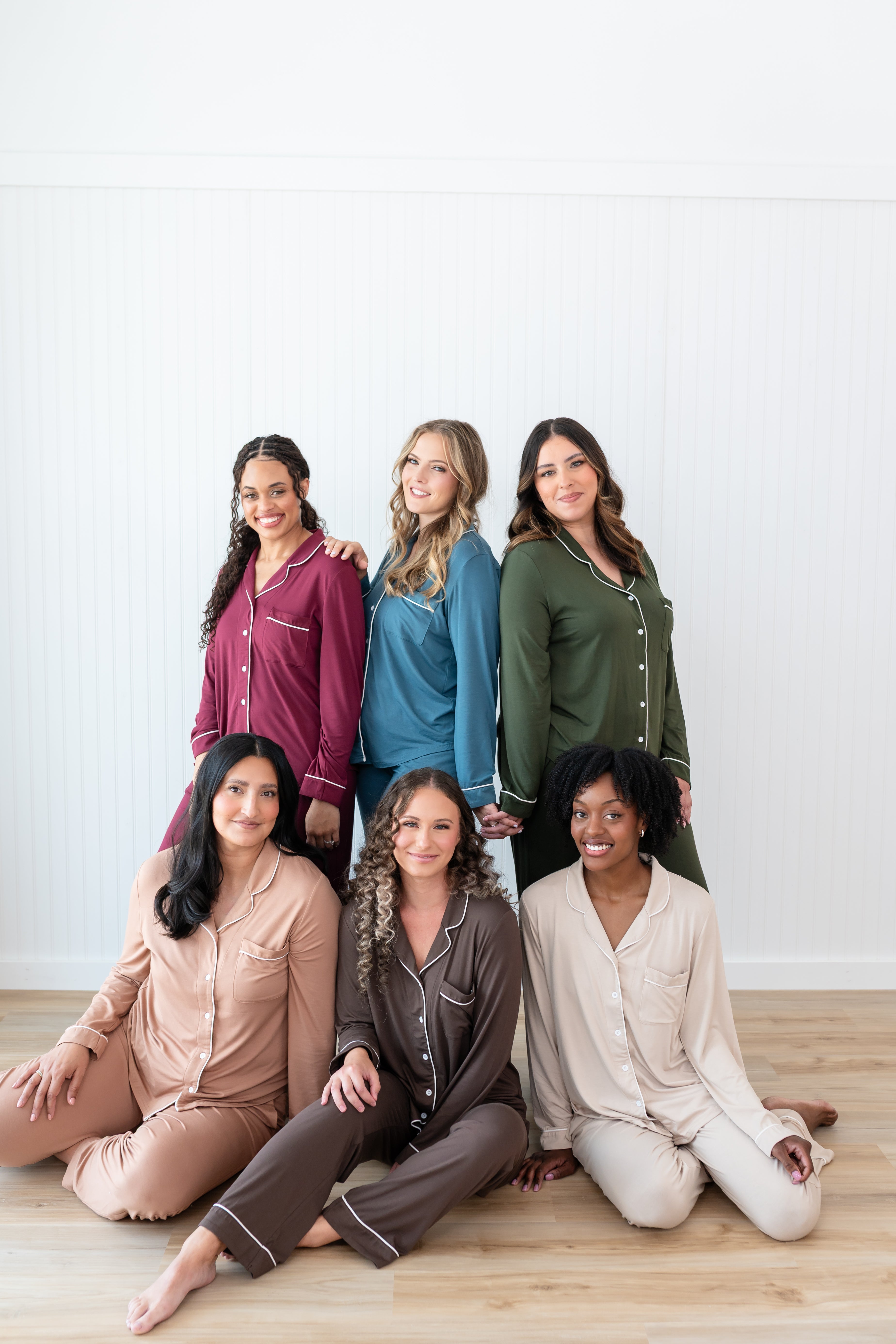 Models standing and sitting in a group wearing Women's Long Sleeve Pajama Sets in Burgundy, Atlantic, Fir, Latte, Espresso and Bisque