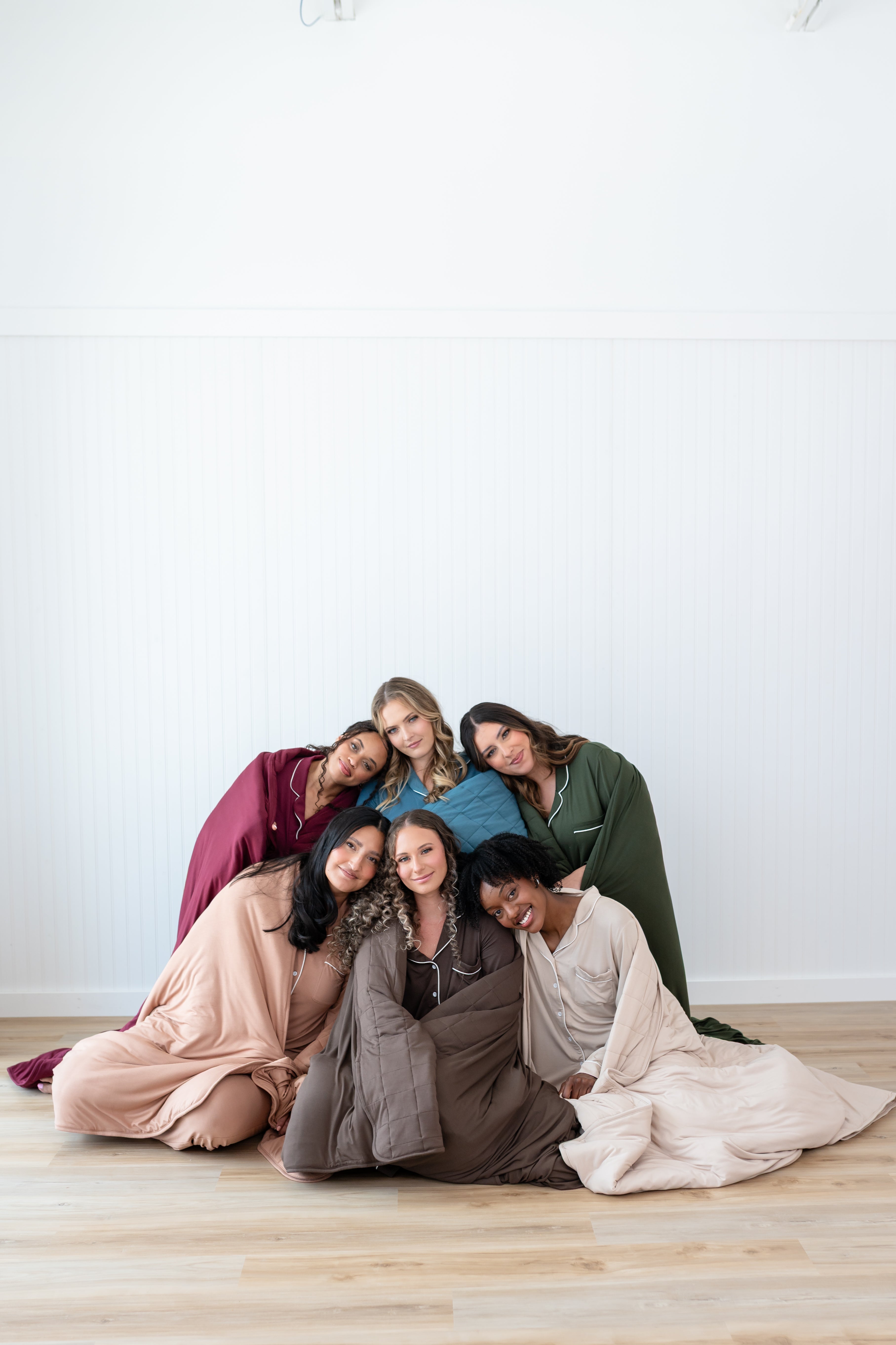 Models sitting together wrapped in Quilted Blankets 2.5 in Burgundy, Atlantic, Fir, Latte, Espresso and Bisque
