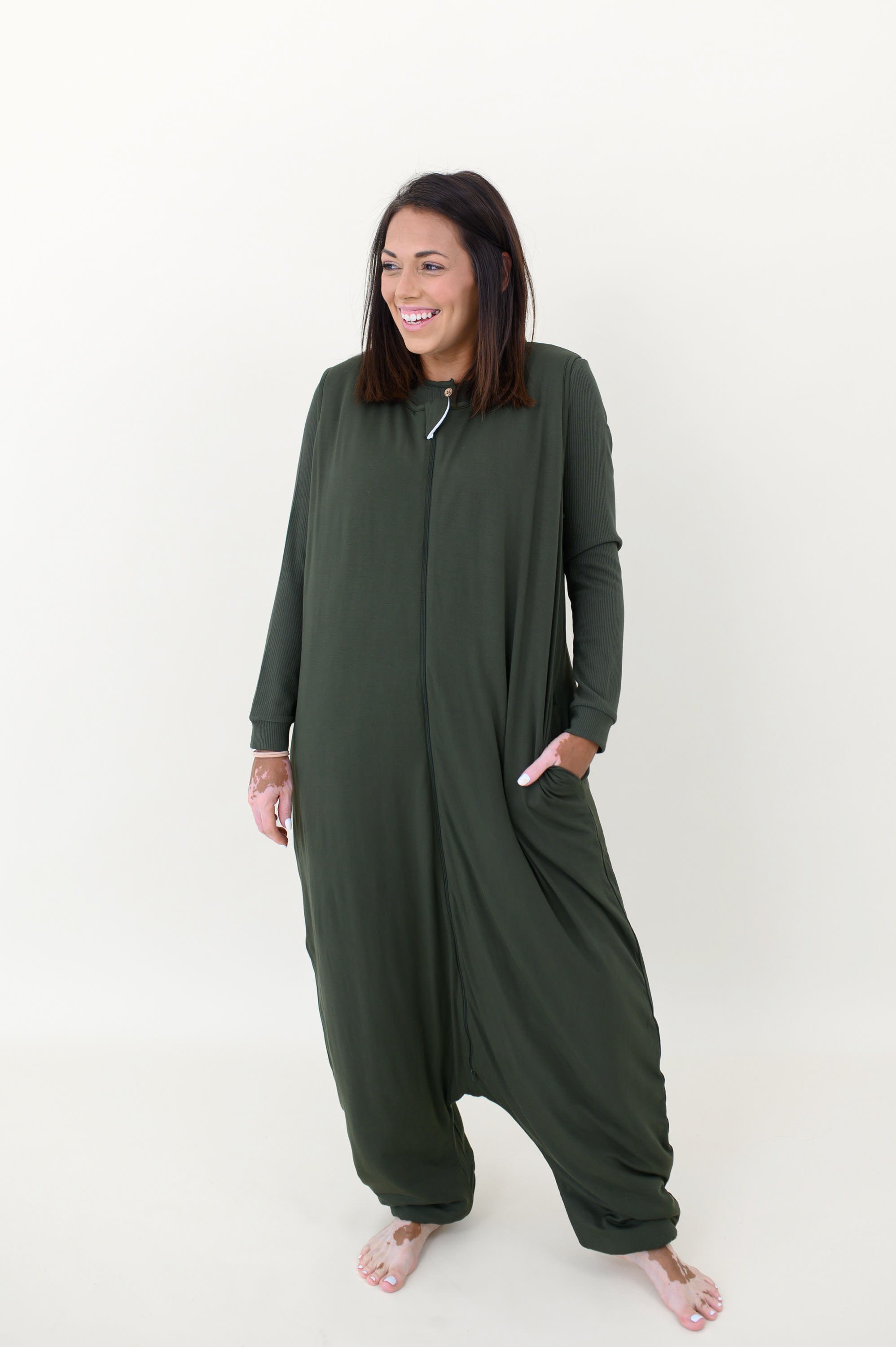 Model laughing while looking to the side and wearing the Adult Sleep Bag Walker in Fir with hand in pocket